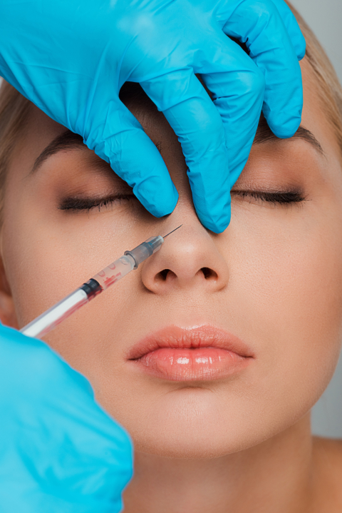 cropped view of beautician in latex gloves holding syringe near nose of girl with closed eyes