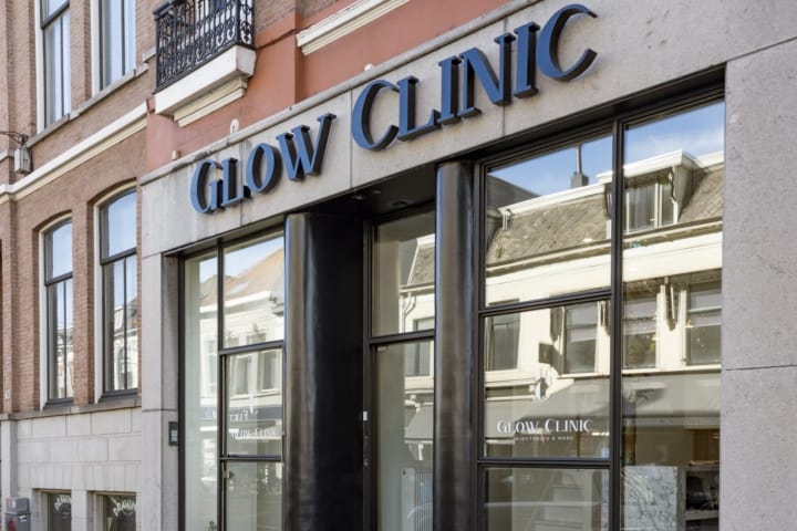 Voorgevel van Glow Clinic met duidelijk zichtbaar logo boven de zwarte toegangsdeur, gevestigd in een klassiek gebouw in Breda, met grote ramen en een reflectie van de straat.