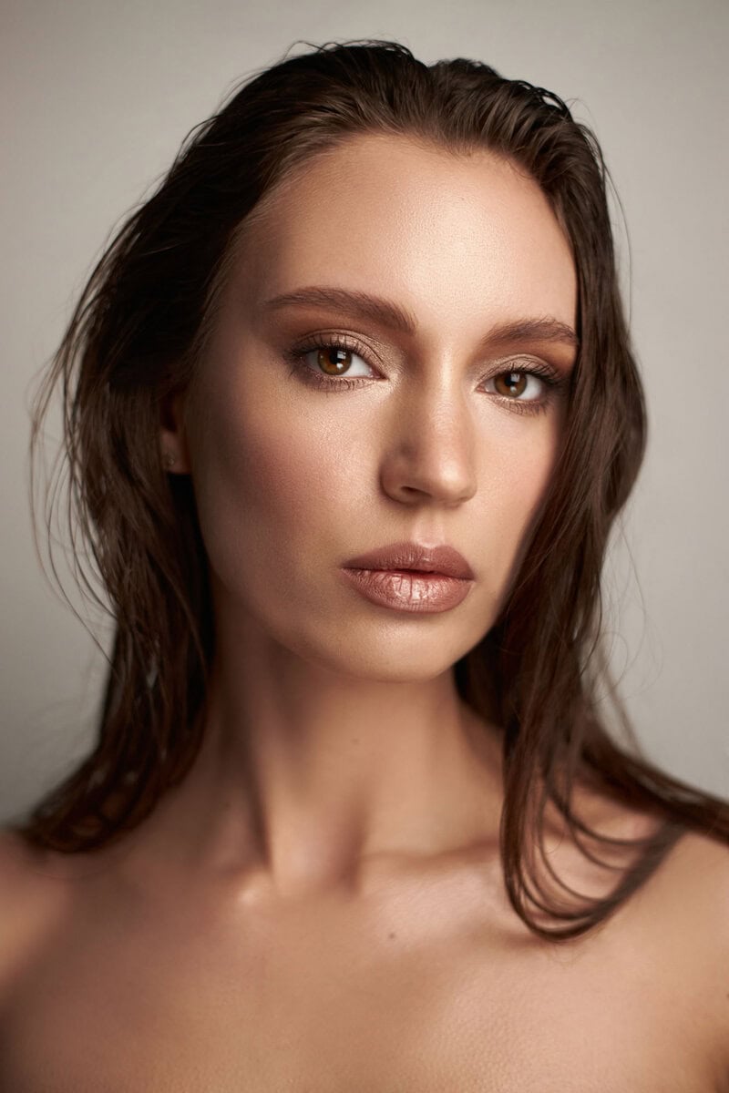 model showcases a fresh makeup look with glowing skin and defined features, captured in soft lighting. focus is on her expressive gaze and natural beauty, enhancing her elegance